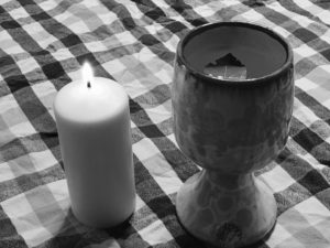 Lit candle and chalice of lustral water with floating bay leaf.